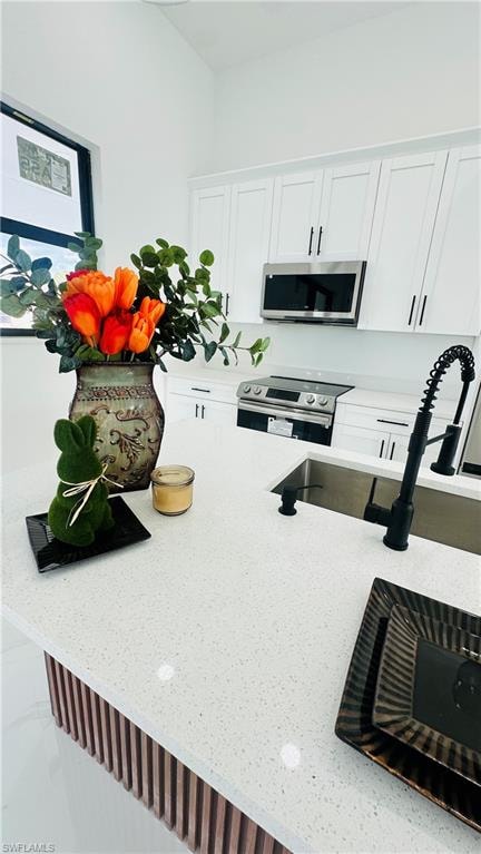 Kitchen with white cabinets, stainless steel appliances, and light stone countertops