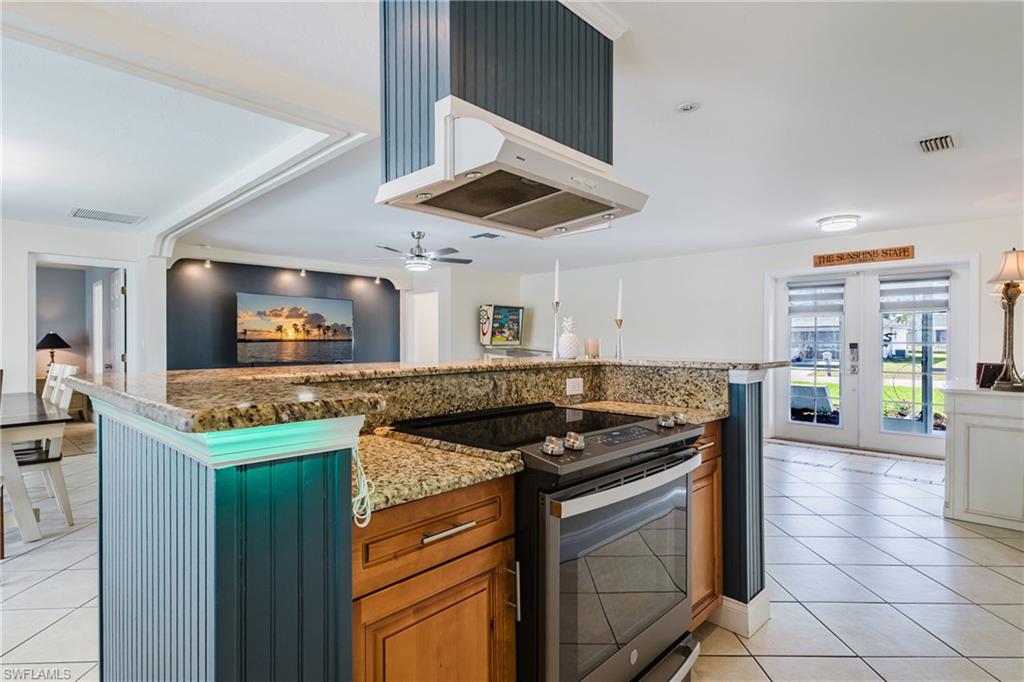 Kitchen with electric stove, wood finish cabinetry, light stone countertops, and ventilation hood