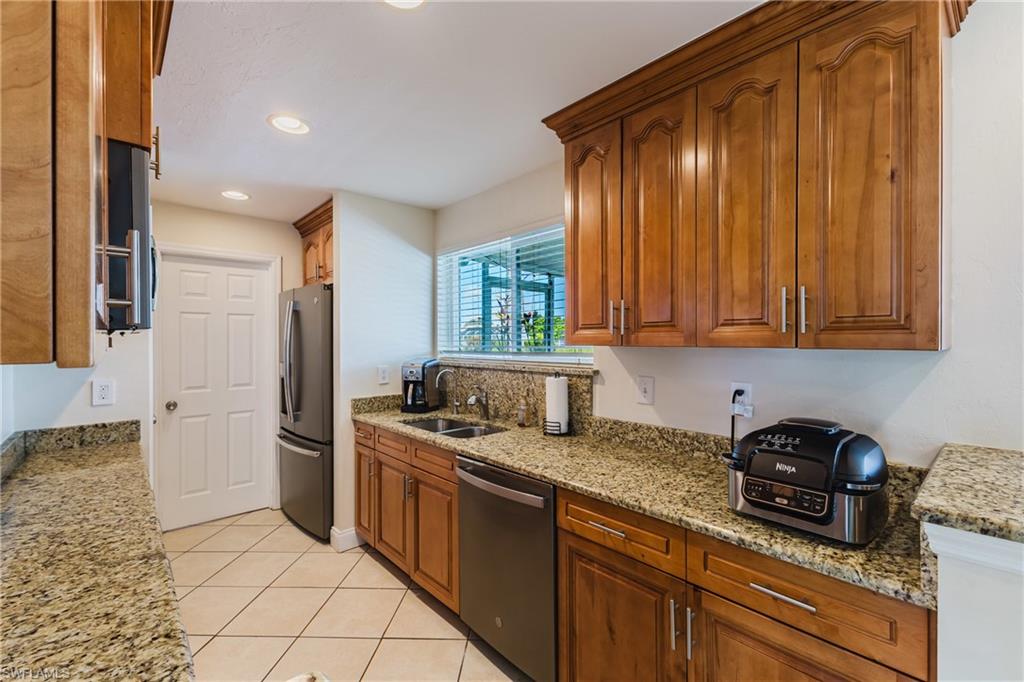 Kitchen featuring wood finish cabinetry, light stone counters, stainless steel appliances, light tile patterned floors, and recessed lighting