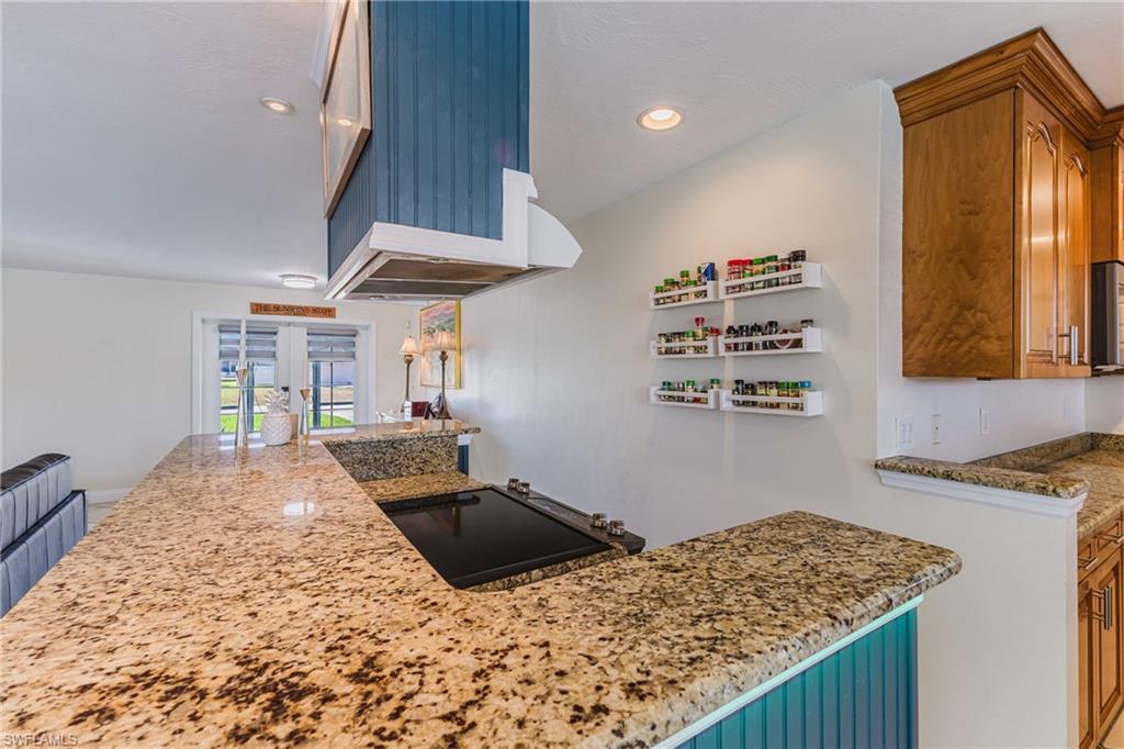 Kitchen with light stone countertops, recessed lighting, black electric cooktop, wood finish cabinetry, and french doors