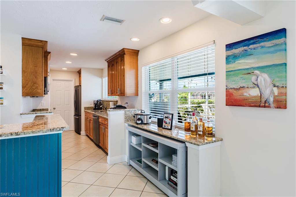 Kitchen featuring light stone counters, recessed lighting, wood finish cabinets, light tile patterned flooring, and freestanding refrigerator