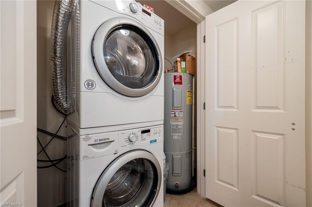 Laundry area featuring electric water heater, light tile patterned floors, and stacked washer and clothes dryer