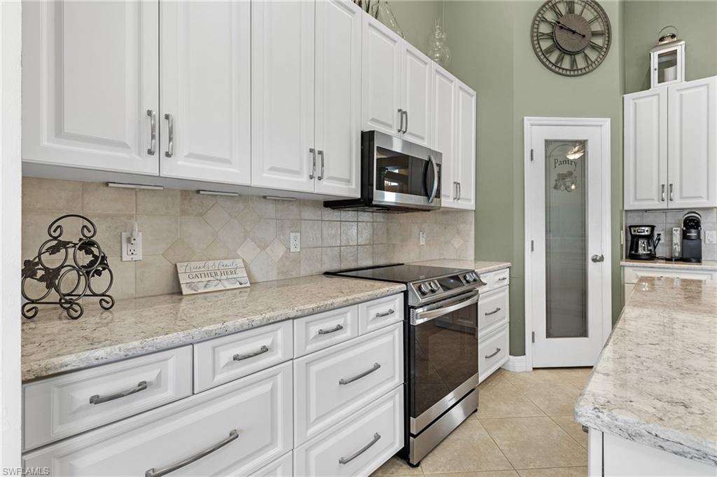 Kitchen featuring appliances with stainless steel finishes, white cabinetry, light stone counters, and decorative backsplash