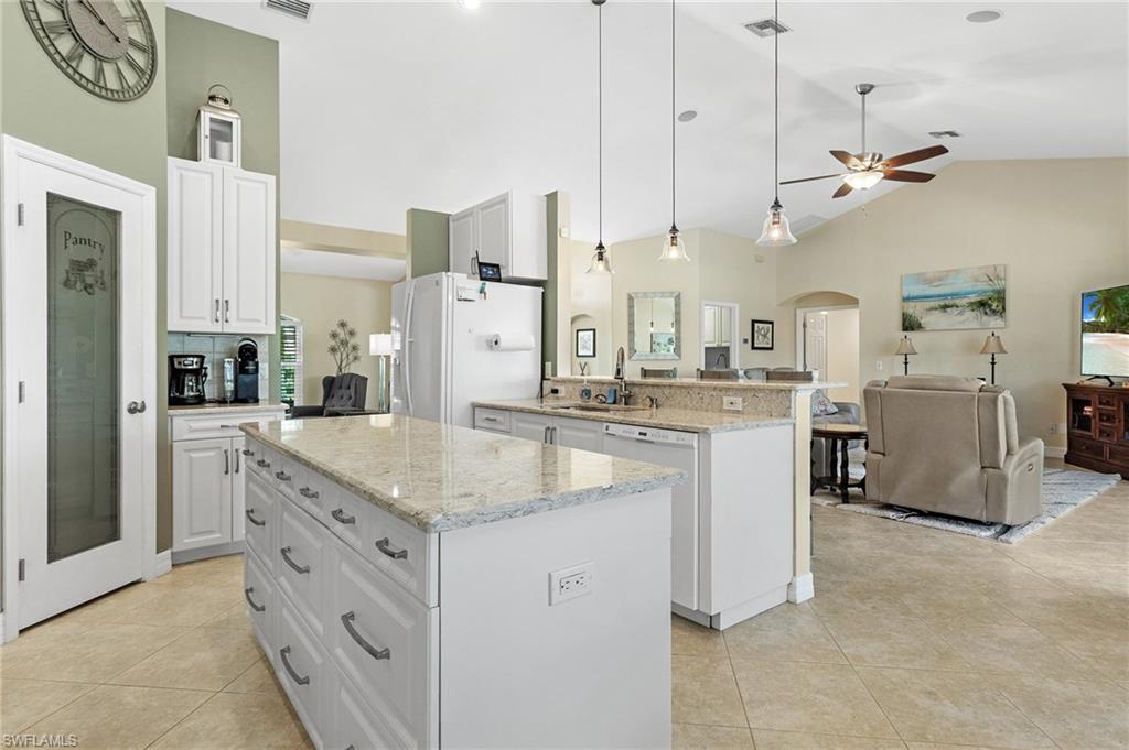 Kitchen featuring white cabinets, high vaulted ceiling, open floor plan, hanging light fixtures, and a center island