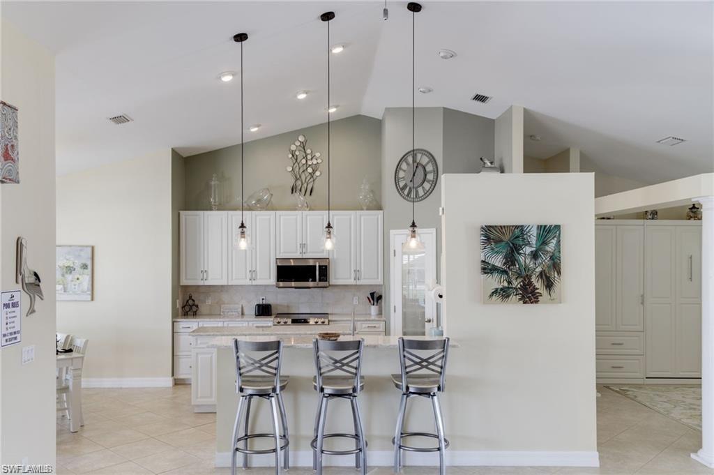 Kitchen with hanging light fixtures, decorative backsplash, light tile patterned floors, appliances with stainless steel finishes, and high vaulted ceiling