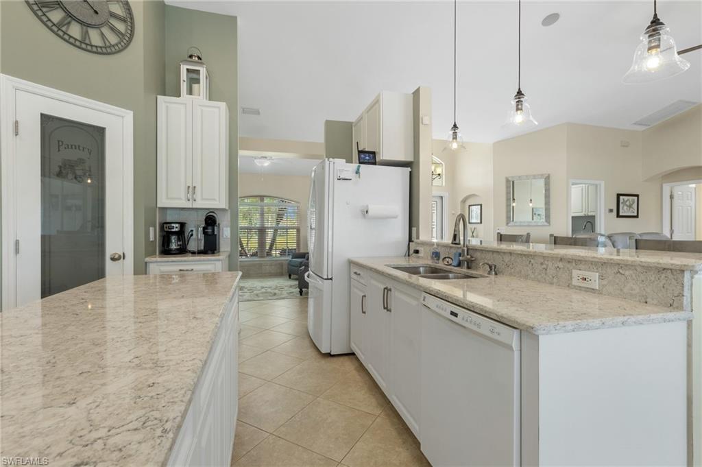 Kitchen with light stone countertops, arched walkways, white appliances, decorative light fixtures, and a peninsula