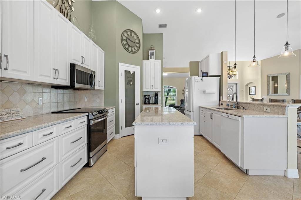 Kitchen featuring stainless steel appliances, decorative light fixtures, a high ceiling, a center island, and light stone counters