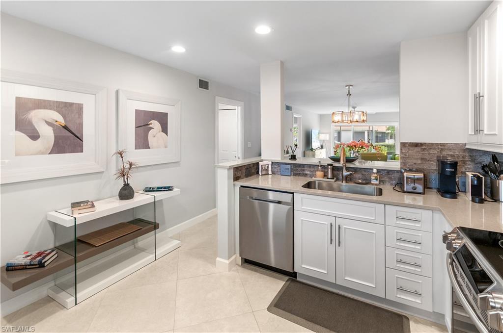 Kitchen with stainless steel appliances, light stone countertops, a chandelier, white cabinets, and a peninsula