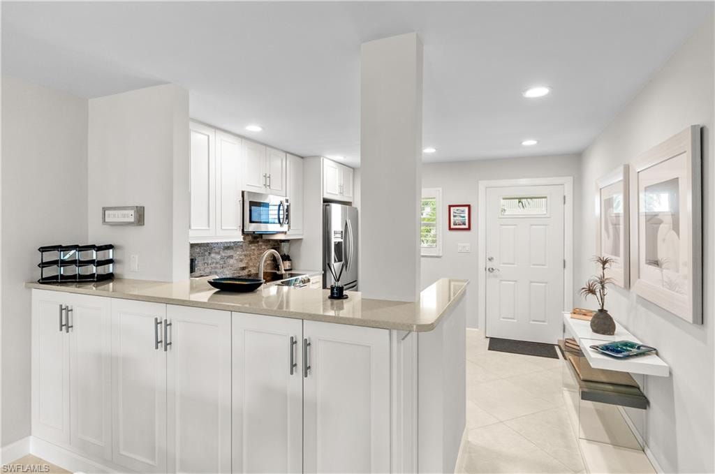 Kitchen with a peninsula, white cabinetry, stainless steel appliances, light stone countertops, and recessed lighting