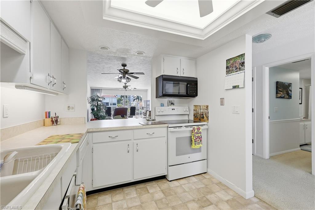 Kitchen featuring white electric stove, a ceiling fan, white cabinetry, light countertops, and black microwave