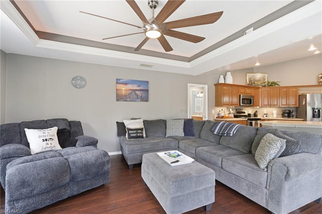 Living area featuring crown molding, a tray ceiling, dark wood finished floors, and ceiling fan