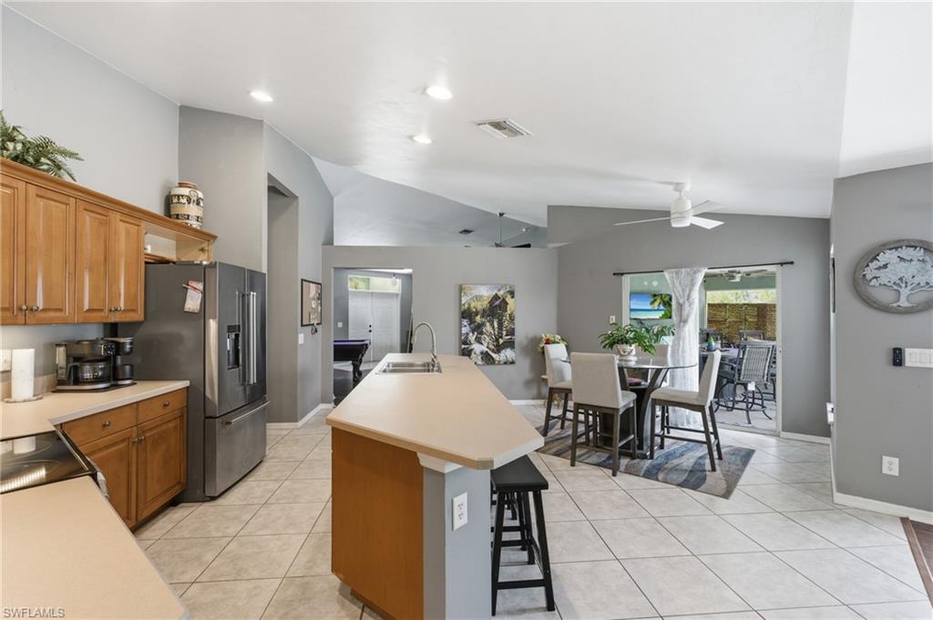 Kitchen with light tile patterned floors, a center island with sink, wood finish cabinets, light countertops, and vaulted ceiling