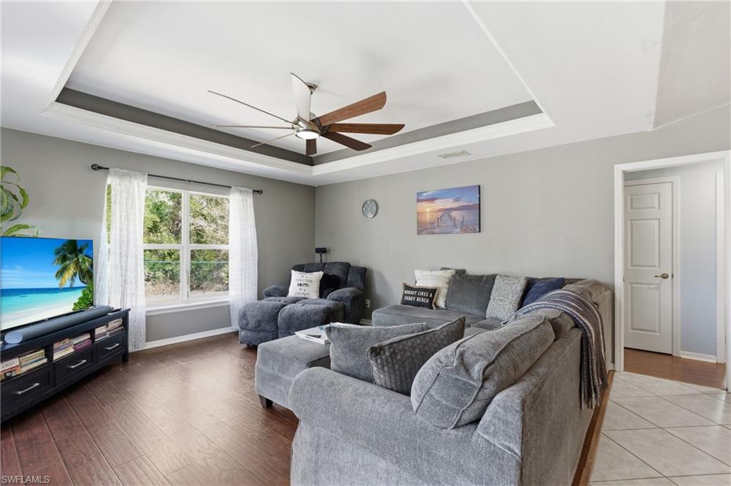 Living area with ceiling fan, a tray ceiling, and wood finished floors