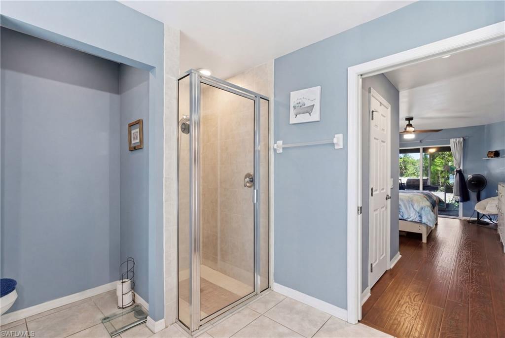 Ensuite bathroom with a stall shower, light tile patterned floors, and a ceiling fan