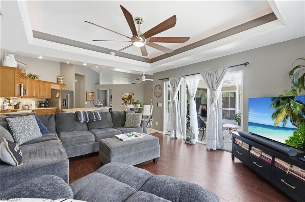 Living area featuring a raised ceiling, dark wood-type flooring, ceiling fan, and crown molding