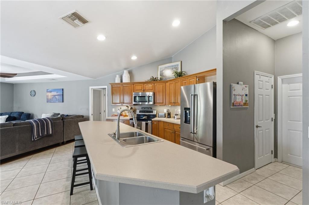 Kitchen with stainless steel appliances, wood finish cabinetry, a kitchen breakfast bar, a kitchen island with sink, and vaulted ceiling