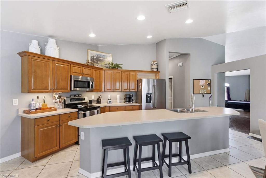 Kitchen with lofted ceiling, light countertops, an island with sink, stainless steel appliances, and wood finish cabinetry