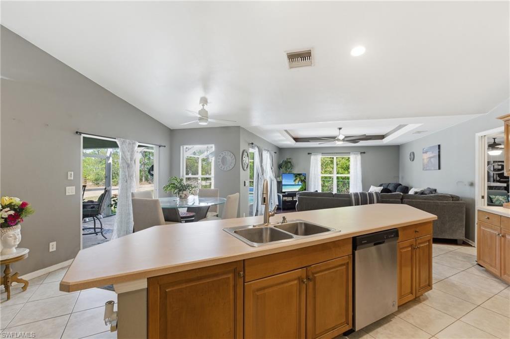 Kitchen featuring open floor plan, light countertops, stainless steel dishwasher, a kitchen island with sink, and a tray ceiling