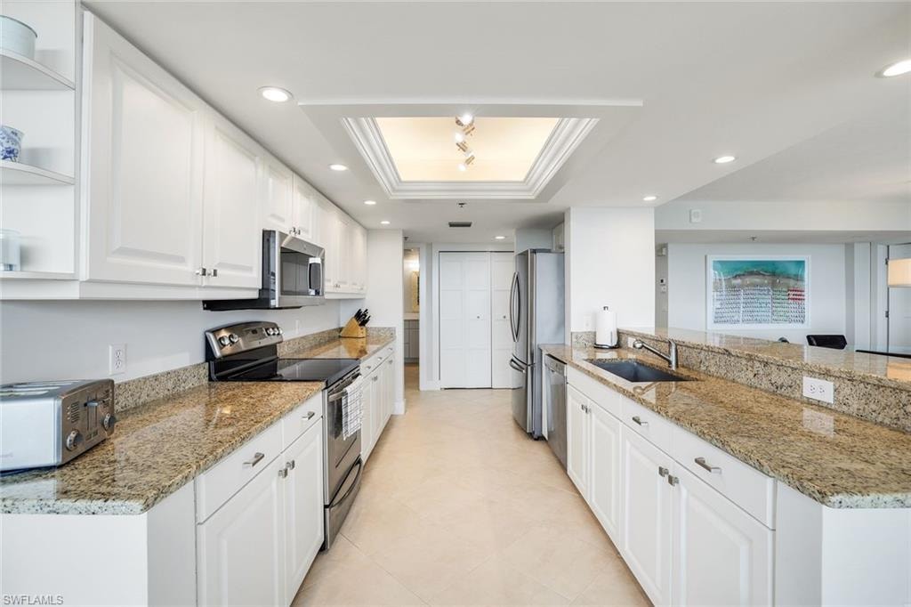 Kitchen with a raised ceiling, white cabinetry, light stone countertops, stainless steel appliances, and crown molding