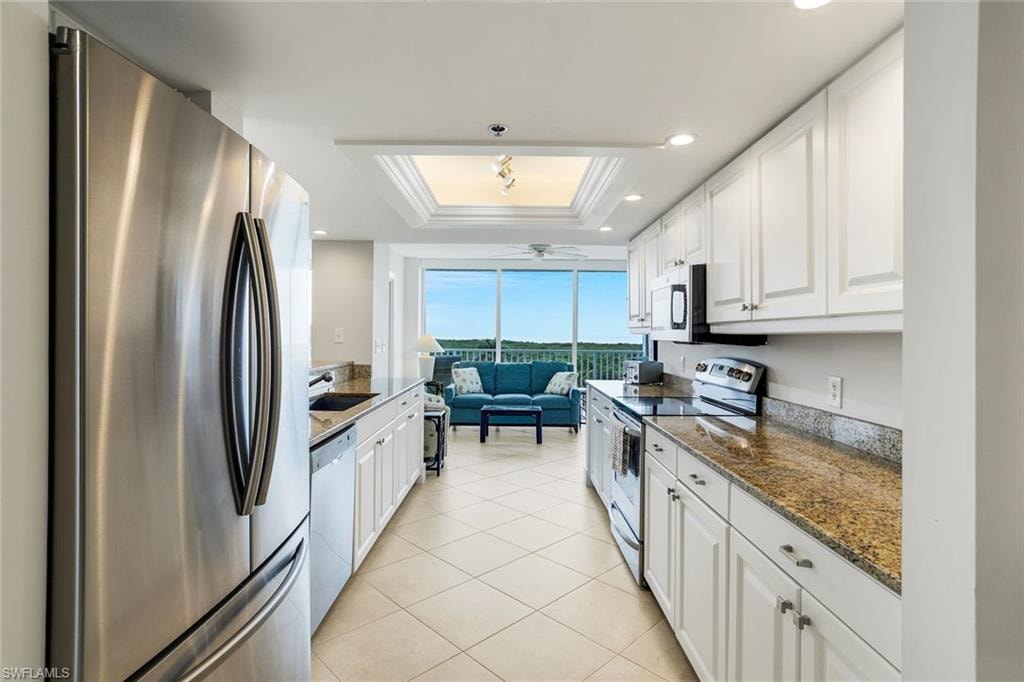 Kitchen featuring stainless steel appliances, white cabinets, a tray ceiling, dark stone countertops, and crown molding