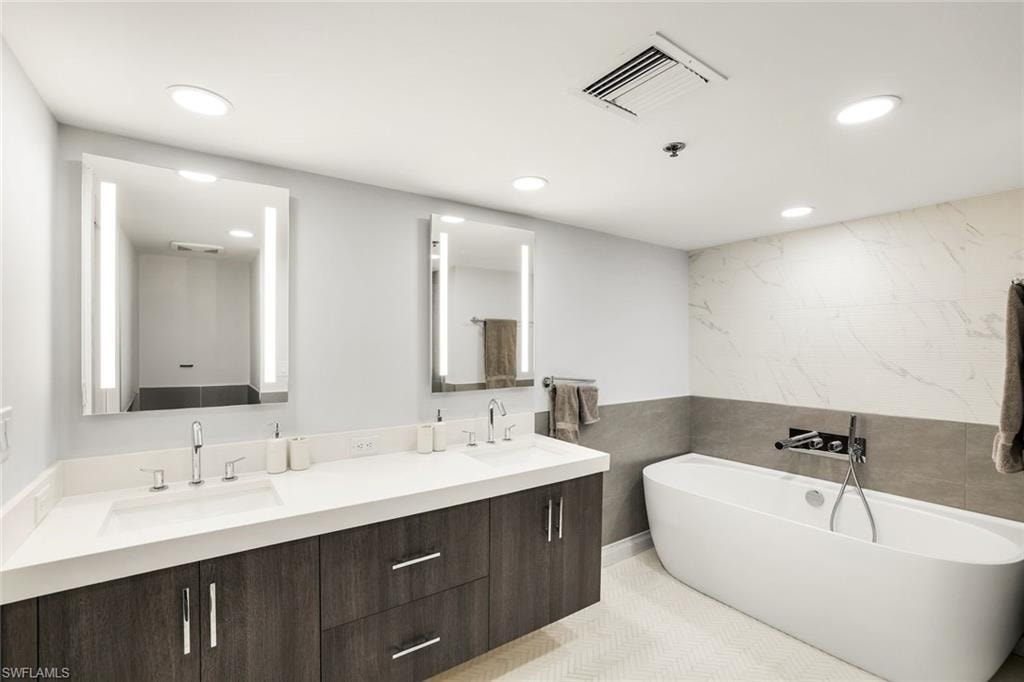 Bathroom with tile walls, double vanity, a freestanding bath, and recessed lighting
