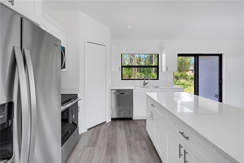Kitchen with stainless steel appliances, white cabinets, light wood-type flooring, and light stone countertops