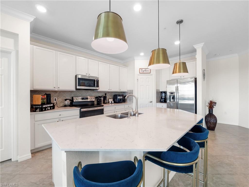 Kitchen with backsplash, ornamental molding, stainless steel appliances, a kitchen bar, and white cabinets