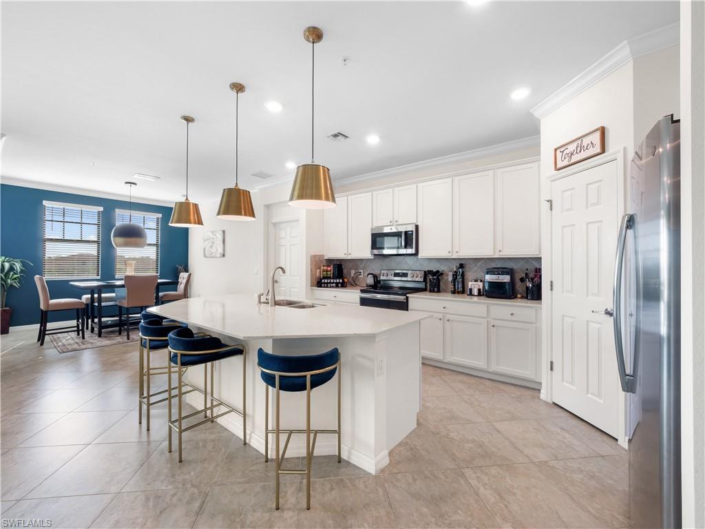 Kitchen with a breakfast bar area, stainless steel appliances, crown molding, an island with sink, and decorative backsplash