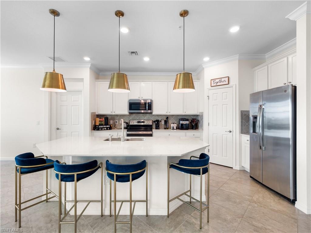 Kitchen featuring stainless steel appliances, a kitchen breakfast bar, crown molding, an island with sink, and white cabinets