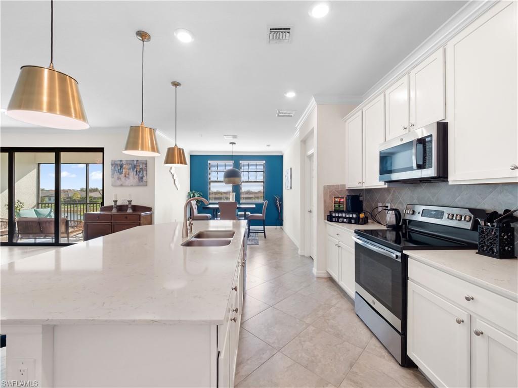 Kitchen featuring stainless steel appliances, white cabinetry, a kitchen island with sink, light stone countertops, and tasteful backsplash