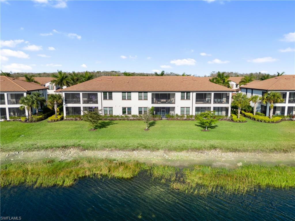 Back of property with a water view, a tile roof, and a lawn