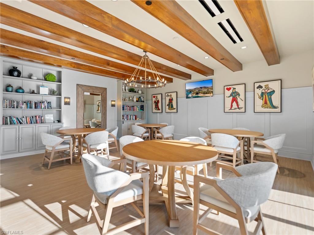 Dining area with beam ceiling, suspended lighting, a decorative wall, light wood finished floors, and built in features