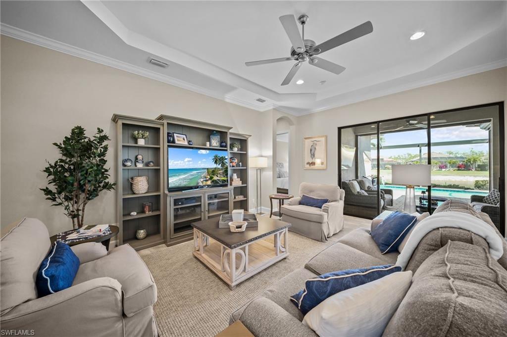 Living room with arched walkways, a raised ceiling, a ceiling fan, crown molding, and recessed lighting