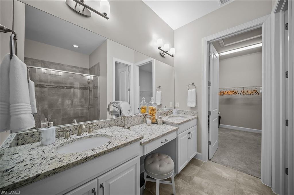 Full bathroom featuring double vanity, a stall shower, a walk in closet, and light colored carpet