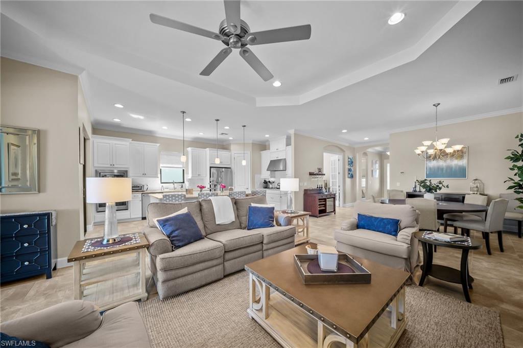 Living room featuring crown molding, a chandelier, a ceiling fan, and a tray ceiling