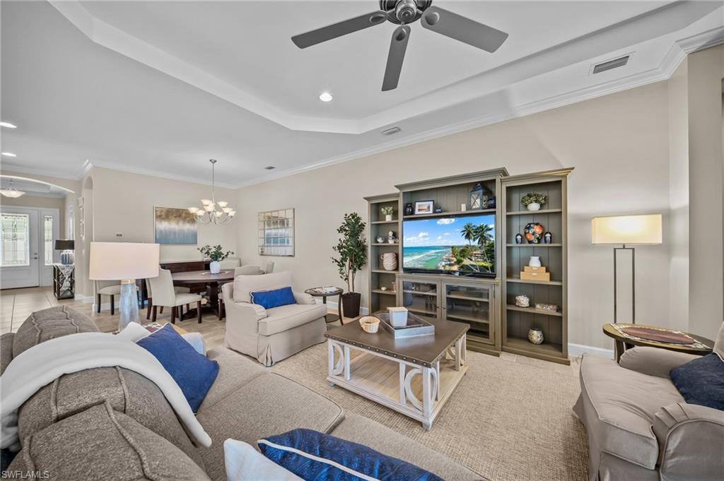 Living area featuring ornamental molding, ceiling fan, suspended lighting, a tray ceiling, and arched walkways