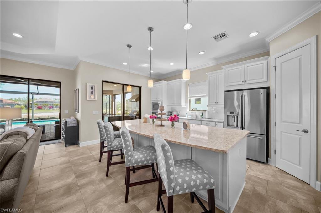 Kitchen featuring high quality fridge, white cabinets, a breakfast bar area, a center island with sink, and light stone countertops