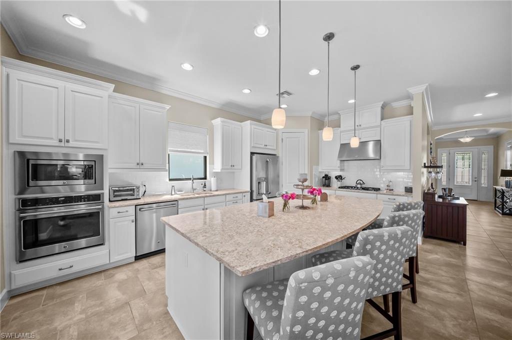 Kitchen featuring stainless steel appliances, white cabinetry, a kitchen bar, a large island, and ornamental molding