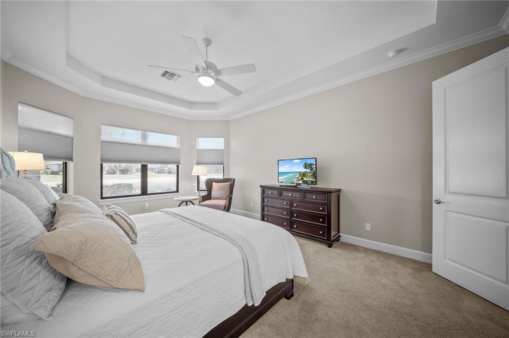 Carpeted bedroom with a raised ceiling, crown molding, and ceiling fan