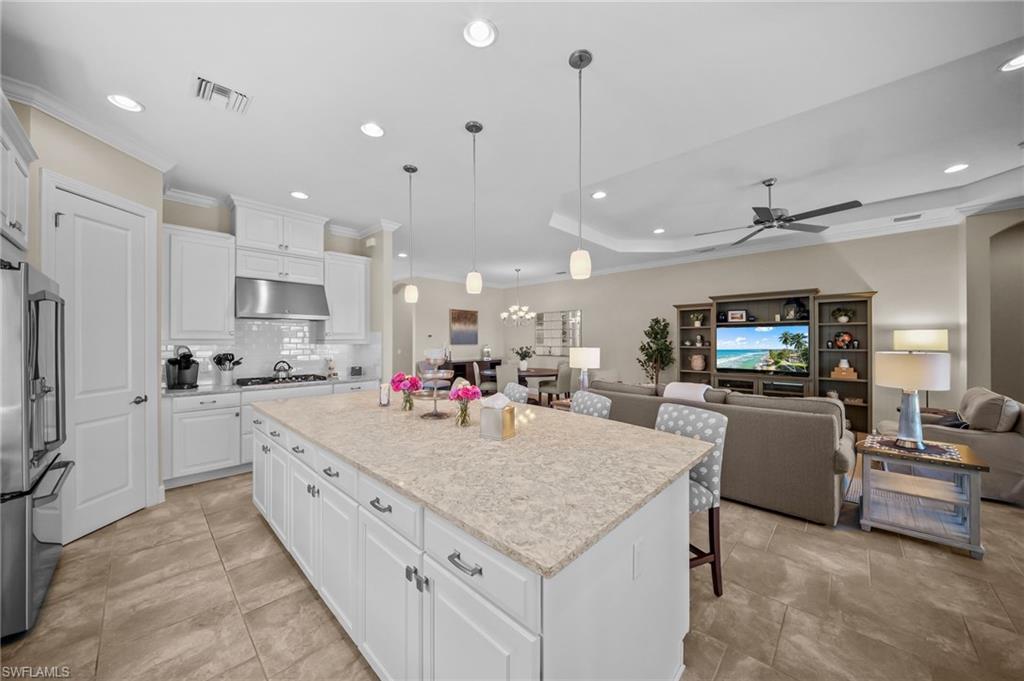Kitchen featuring open floor plan, white cabinets, stainless steel appliances, ornamental molding, and a raised ceiling