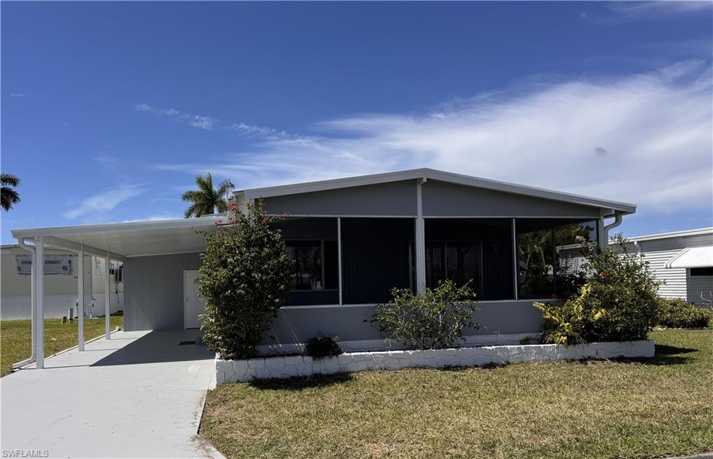 Manufactured / mobile home with a front lawn, an attached carport, driveway, shed, and a sunroom