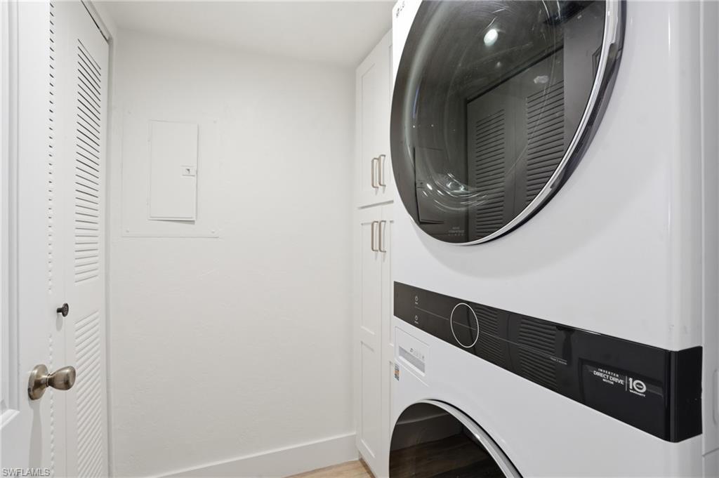 Very Spacious Laundry room with stacked washing machine and dryer, cabinet space, light wood finished floors, and electric panel - Virtually Edited Image