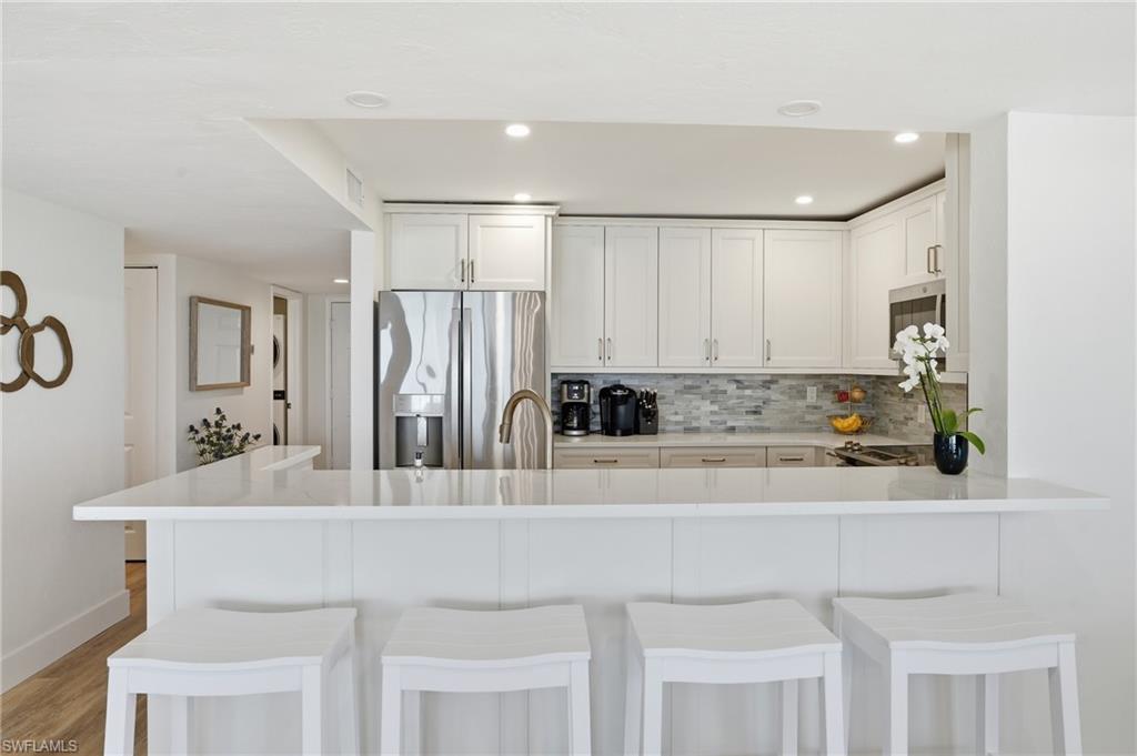 Kitchen with a peninsula, stainless steel appliances, a breakfast bar, white cabinetry, and recessed lighting - Virtually Edited Image