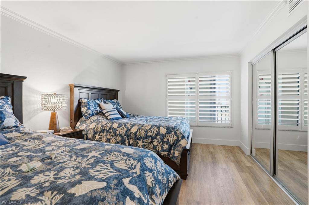 Bedroom featuring light wood finished floors, crown molding, and a closet - Virtually Edited Image