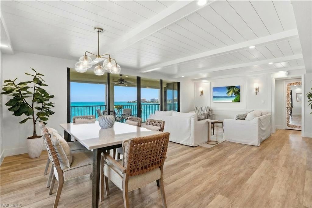 Open-concept living and dining area featuring wide-plank wood-finish flooring, a shiplap ceiling, and extensive floor-to-ceiling sliding glass doors opening to a covered balcony - Virtually Edited Image