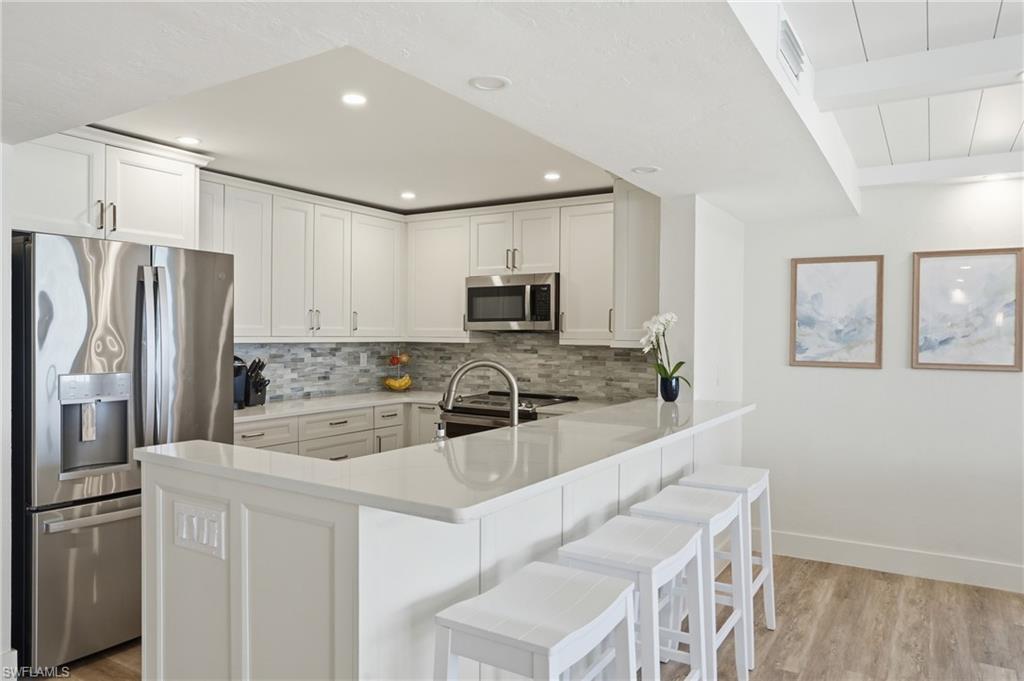 Kitchen featuring stainless steel appliances, white cabinetry, light wood finished floors, decorative backsplash, and light stone countertops - Virtually Edited Image