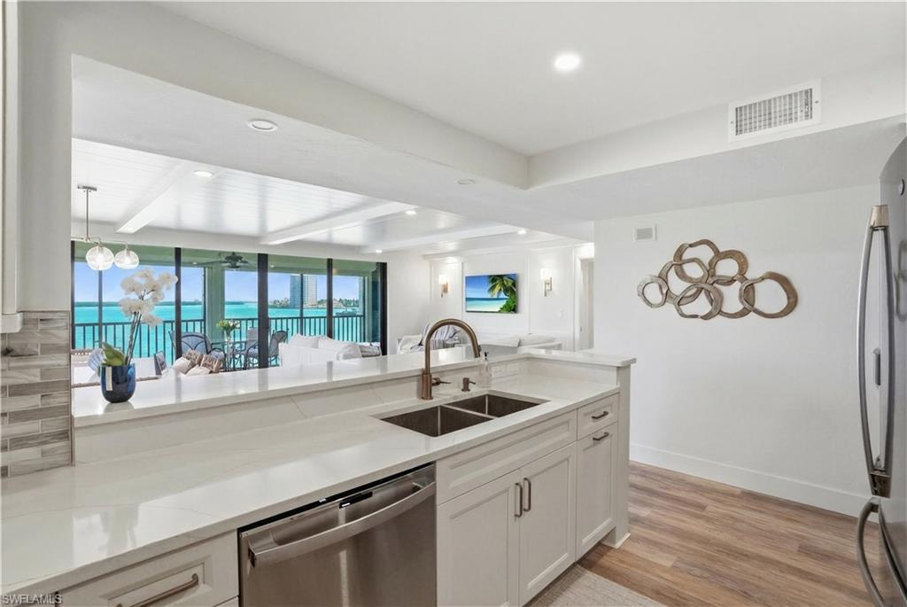 Contemporary kitchen with white cabinetry, stainless steel appliances, and wood-finish flooring - Virtually Edited Image