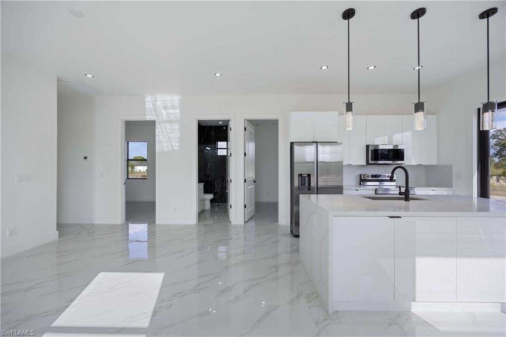 Kitchen with white cabinets, stainless steel appliances, pendant lighting, modern cabinets, and light stone counters