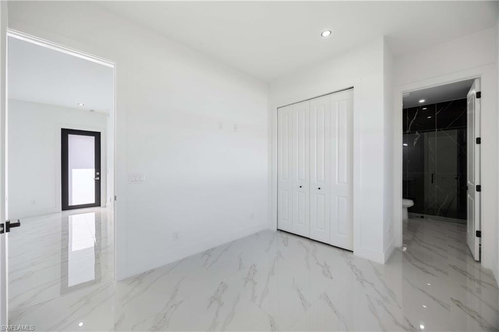 Unfurnished bedroom featuring recessed lighting, a closet, light marble finish floors, and connected bathroom