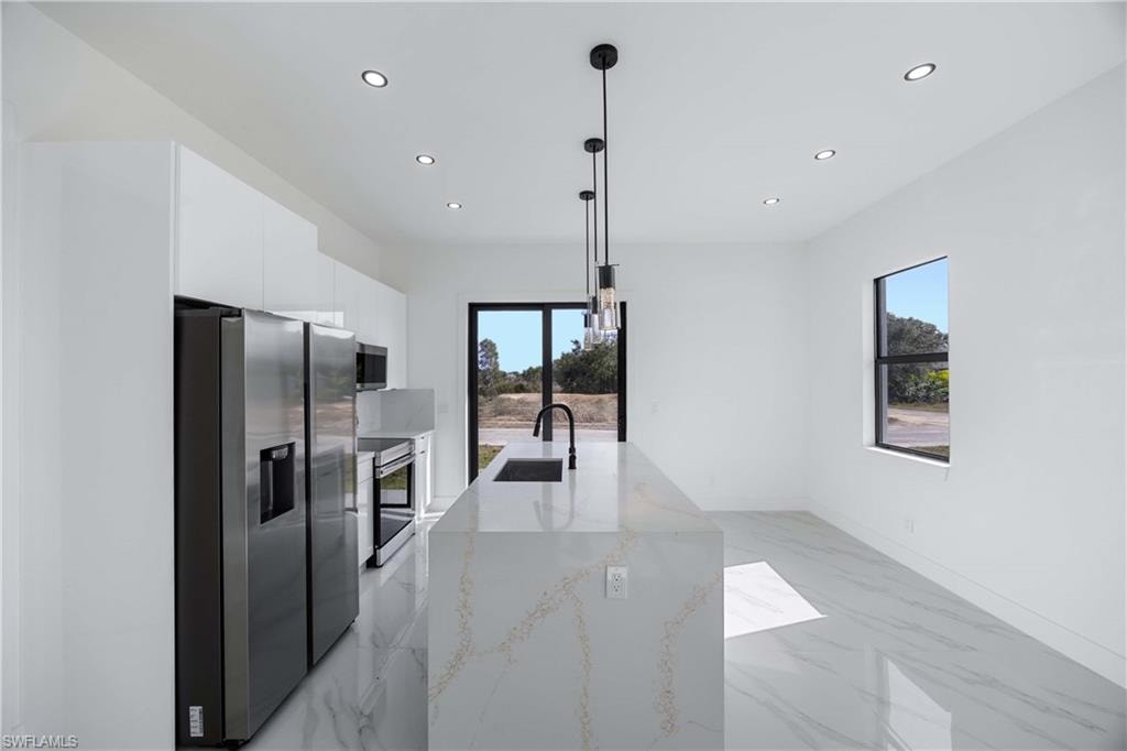 Kitchen featuring stainless steel appliances, white cabinets, light stone counters, modern cabinets, and light marble finish floors